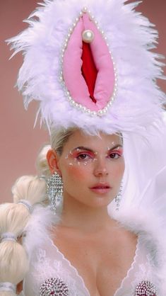 a woman wearing a white feather headdress and pink eyeliners is posing for the camera