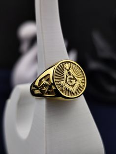 a gold masonic ring on top of a white stand with the masonic symbol in it