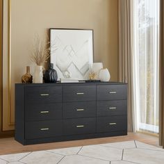 a black dresser with two vases on top of it next to a large window