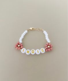 a pink and white beaded bracelet with the word mom written on it in gold letters