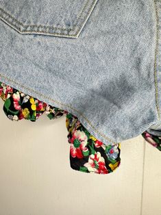 a pair of blue jean shorts with floral print on the bottom and side, hanging from a hook