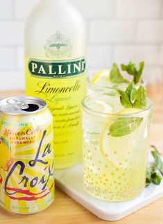 a bottle of lemonade next to a glass filled with ice and mint on a tray