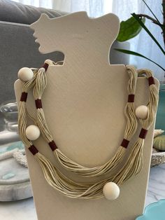 a necklace with beads and wooden beads on a display stand next to a potted plant