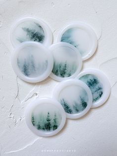 four coasters with trees printed on them sitting on a white surface, in the shape of circles