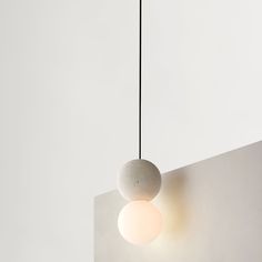 a white ball hanging from a black cord next to a light fixture on a wall