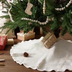 a christmas tree with presents under it on a wooden floor next to a white knitted blanket