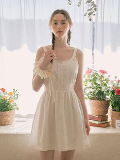 a woman standing in front of a window holding an umbrella and wearing a white dress