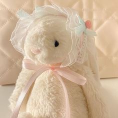 a white teddy bear with a pink ribbon around it's neck sitting on a bed