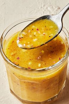 a spoon with some food in it on a white counter top next to a glass jar filled with liquid