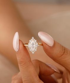 a woman's hand holding a ring with a diamond on it and pinkish nails