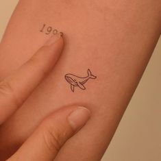 a small tattoo on the arm of a woman's left hand, depicting a whale