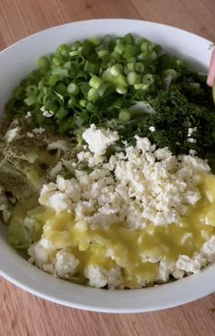 a white bowl filled with different types of food on top of a wooden table next to a person's hand