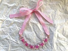 a pink and white checkered ribbon is attached to a necklace on a piece of paper