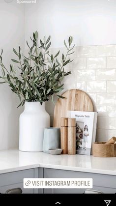 a white kitchen counter top with an olive plant in a vase and magazines on it