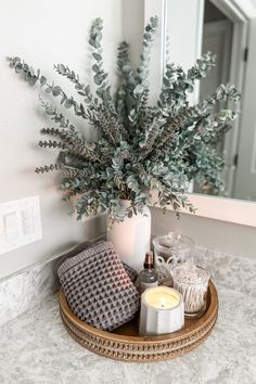 a tray with candles, blankets and a vase filled with greenery sits on a bathroom counter