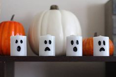 three candles with faces painted on them sit in front of pumpkins and a white pumpkin