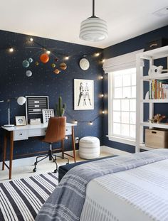 a bedroom decorated in blue and white with planets on the wall, lights strung from the ceiling