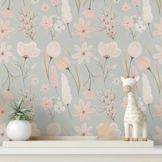 a giraffe figurine sitting on top of a shelf next to a flower wallpaper