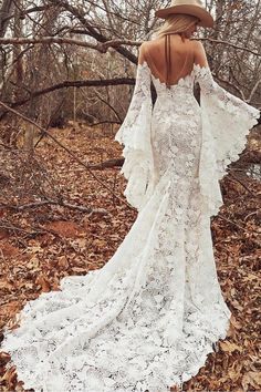 a woman in a white dress and hat standing in the woods with her back to the camera