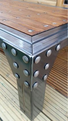 a wooden table with metal rivets sitting on top of a wooden floor next to a bench