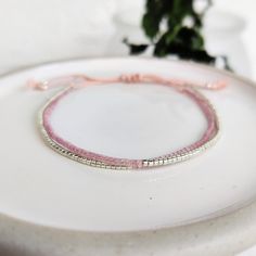 This delicately-strung exclusively crafted bracelet has two strands of tiny Japanese Miyuki glass beads in pink Shell Silk and shiny silver set on natural light pink silk cord. All beads have  a uniform shape with a sparkly finish, perfect for a minimalist look that can be dressed up or down. Finished with a macramé sliding clasp to adjust to your size. **New** Now available with Silver or Gold beads. Please select from variations Also available in Gold/Shell or Turquoise/Copper - https://www.et Small Jute Bags, Copper Glass, Dainty Bracelet, Holiday Essentials, Silk Cord, Jute Bags, Bracelets Handmade Beaded, Glass Beaded Bracelets, Dainty Bracelets