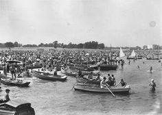 an old black and white photo of many boats in the water with people on them