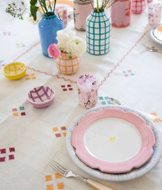 the table is set with pink and blue plates, cups, and flowers in vases