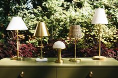 three lamps sitting on top of a green table next to bushes and trees in the background