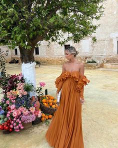 a woman in an orange dress standing next to a tree with flowers on the ground