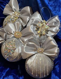 four silver ornaments with bows and jewels on them are sitting on a blue velvet surface