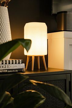 a white lamp sitting on top of a wooden table next to a book and plant