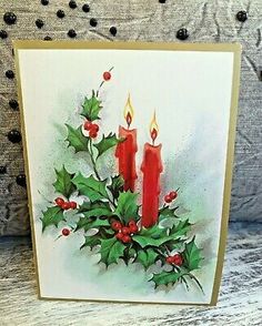 a christmas card with two red candles and holly berries on it, sitting on a table