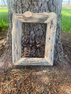 a wooden frame hanging on the side of a tree in front of a grass field