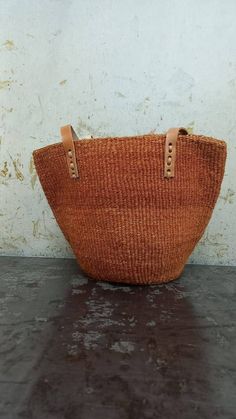 "Unique and stylish burned orange sisal kiondo bag with stitched leather straps. Ideal as a beach bag, shopping basket, market basket or storage basket. This unique tote bag is handmade by a group of ladies in a remote rural village in Machakos, Kenya. Do not clean with water. If the bag gets wet, please dry to avoid dampness.  Leather type used is bovine, from cattle. It's natural and in it's purest form. DIMENSIONS Bottom width: 10\"/25.5cm Top width: 14\"/35.56cm Depth: 10\"/25.5cm Straps: 15\"/38cm SHIPPING All orders ship via DHL Express (3-5) days delivery time." Woven Natural Fiber Basket Bucket Bag, Eco-friendly Orange Rectangular Straw Bag, Woven Basket Bucket Bag In Natural Color, Natural Woven Basket Bucket Bag, Casual Brown Woven Bucket Bag, Casual Brown Basket Bag, Basket-shaped Bucket Bag In Woven Leather And Jute, Brown Bohemian Straw Tote Bag, Casual Brown Basket Straw Bag