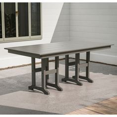 a wooden table sitting on top of a cement floor next to a white wall and windows