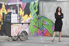 a woman standing in front of a food cart with an umbrella over her head and graffiti on the wall behind her