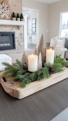 candles are sitting on a tray with pine cones and evergreen branches in front of a fireplace