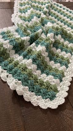 a green and white crocheted afghan on a wooden floor next to a vase