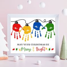 a christmas card with three handprints hanging from the string, next to a small tree