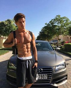 a shirtless man standing in front of a car with his hand on his hip