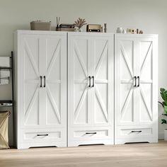 a white armoire with doors and drawers in a room next to a potted plant