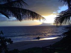 the sun is setting over an ocean with palm trees