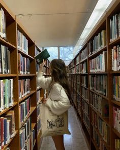 a woman is looking at books in a library and she is holding a bag over her head