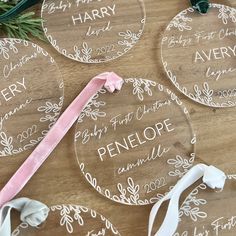 three personalized glass christmas ornaments on a wooden table with greenery and ribbon tied around them