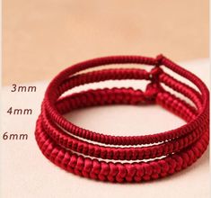 three red rope bracelets on top of a white table next to a measuring tape