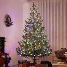 a small christmas tree with multicolored lights in a living room next to presents