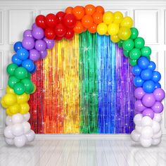 a rainbow arch with balloons and streamers on the floor in front of a white wall