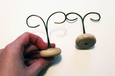 a hand holding a pair of scissors next to two wire sculptures on a white surface