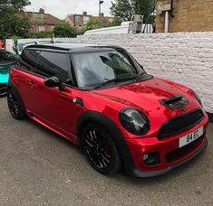 a small red car parked in front of a white brick wall next to other cars