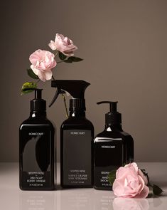 three black bottles with pink flowers in them